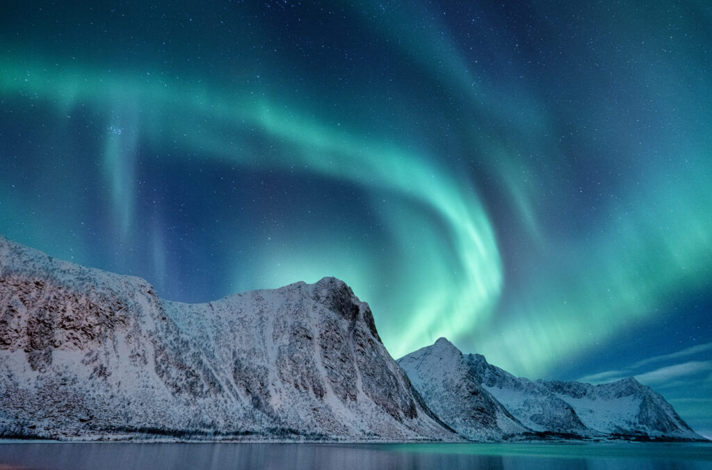 the northern lights in iceland over snowy mountains as seen by Northern lights cruise on Iceland group tour