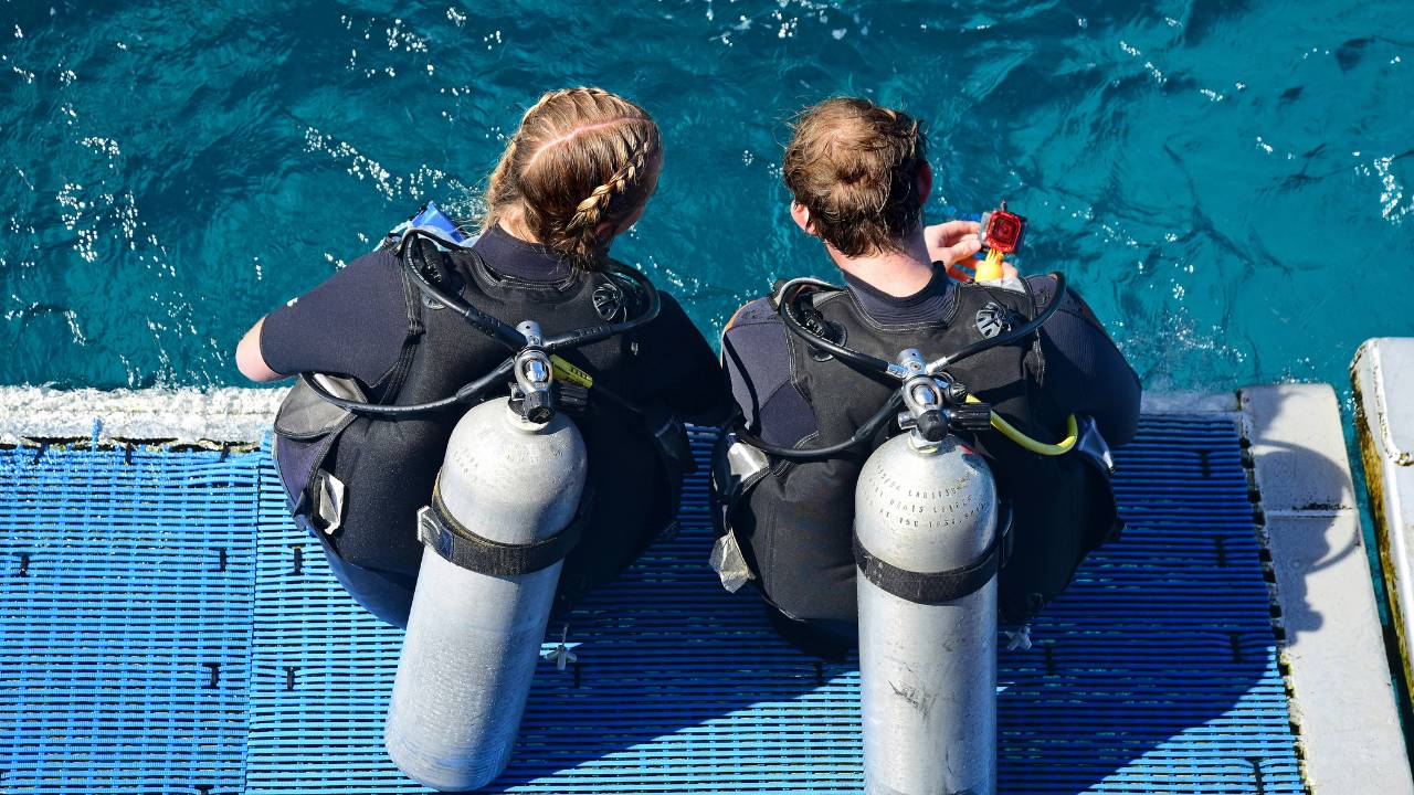 A woman and a man in diving suits preparing to dive into the sea